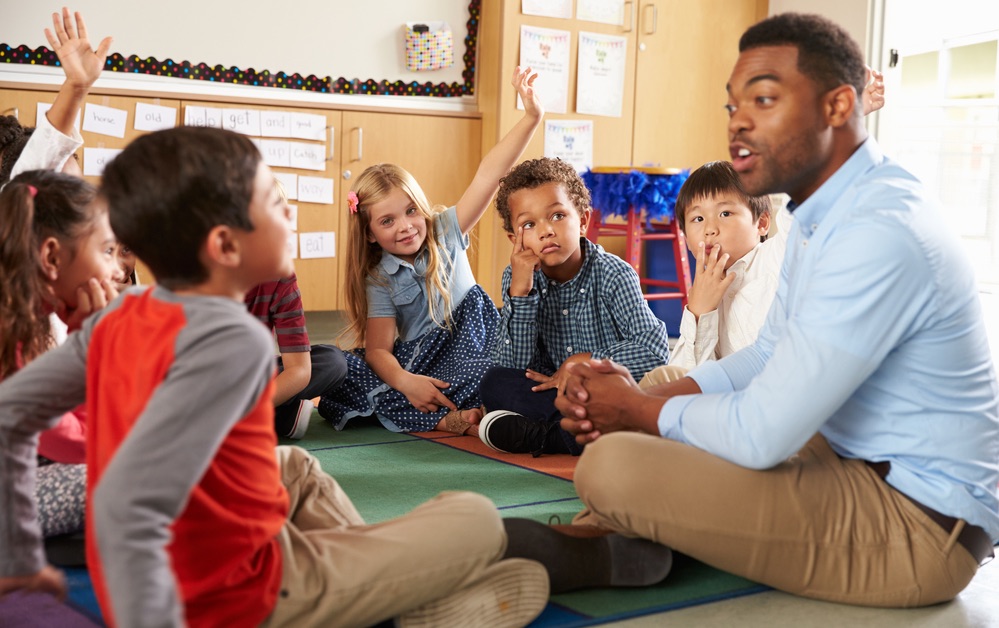African American teacher sitting on the floor with group of students